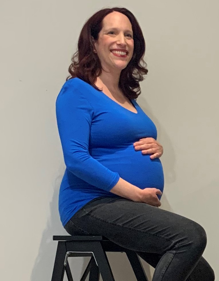 Une femme enceinte souriante, mains sur le ventre